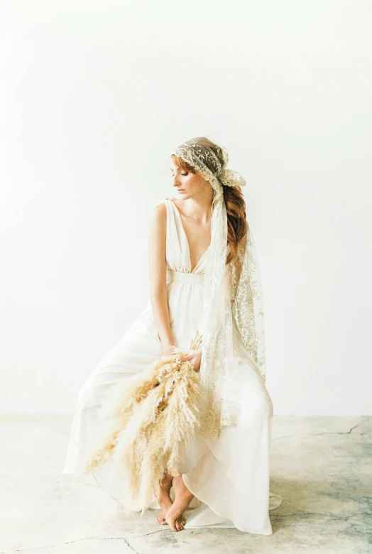 a woman sitting on top of a cement floor, unsplash, renaissance, wearing a wedding dress, wearing wheat yellow gauze, in front of white back drop, bouquet