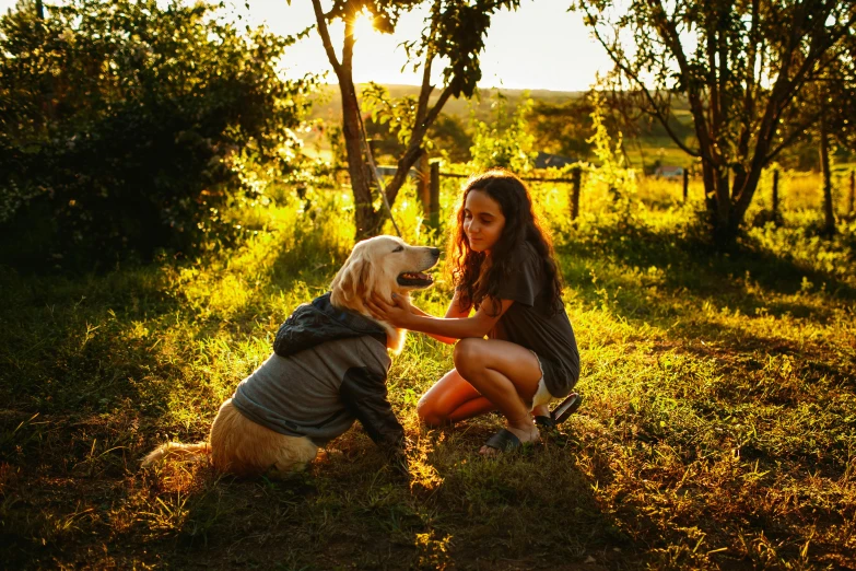 a woman kneeling next to a dog in a field, a picture, by Julia Pishtar, pexels, bright dappled golden sunlight, australian, teenage girl, a handsome