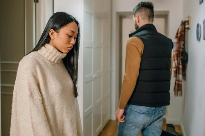 a woman standing next to a man in a hallway, trending on pexels, wearing sweater, breaking apart, asian woman, in small room