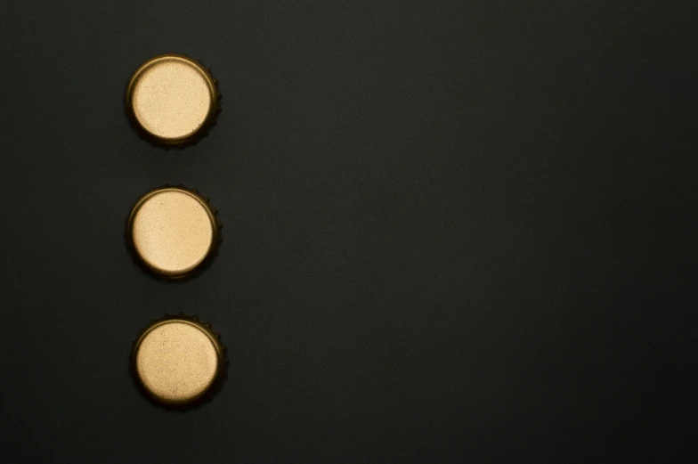 three gold buttons sitting on top of a black surface, by Ottó Baditz, trending on unsplash, minimalism, beer bottle, 15081959 21121991 01012000 4k, panel of black, a high angle shot