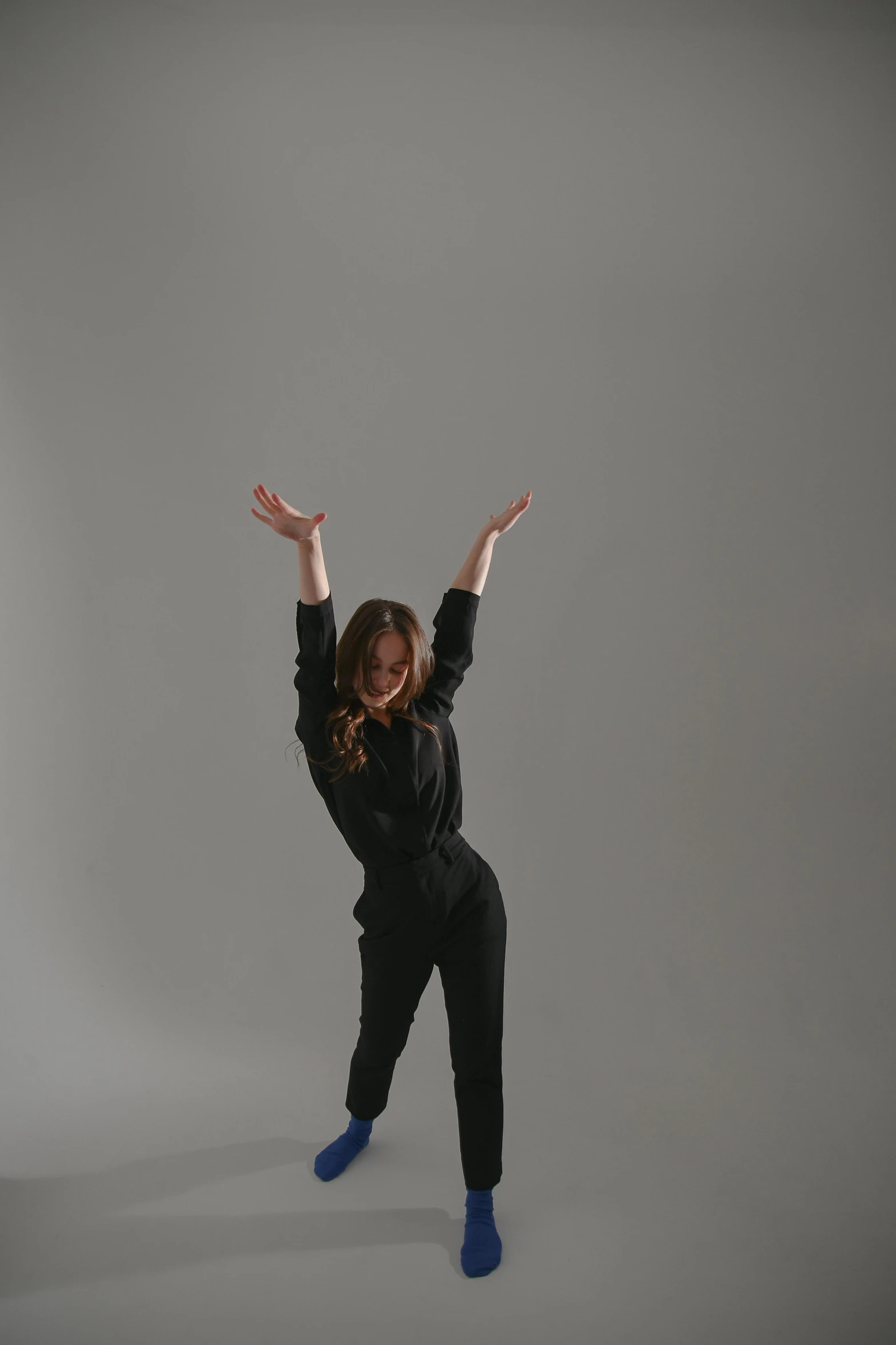 a woman in a black shirt and blue socks, an album cover, inspired by Elizabeth Polunin, unsplash, arabesque, pose(arms up + happy), in a photo studio, wearing a track suit, girl in suit