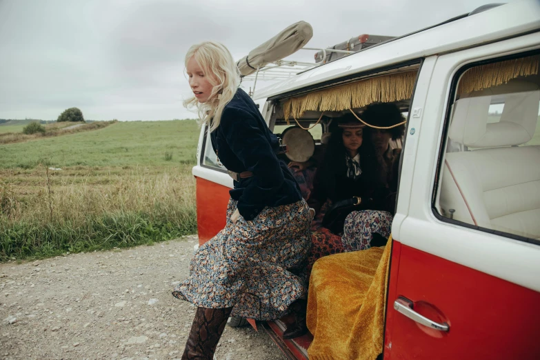 a woman standing next to a red and white van, an album cover, unsplash, kitsch movement, anya taylor - joy and emma stone, wearing dirty travelling clothes, broomstick, vintage clothing