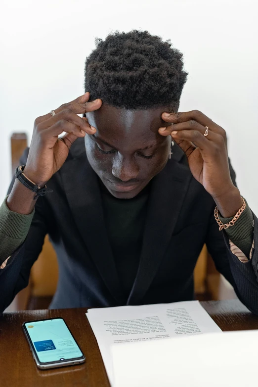a man sitting at a table with his head in his hands, by Barthélemy Menn, pexels contest winner, academic art, adut akech, sitting in dean's office, boy has short black hair, reading new book