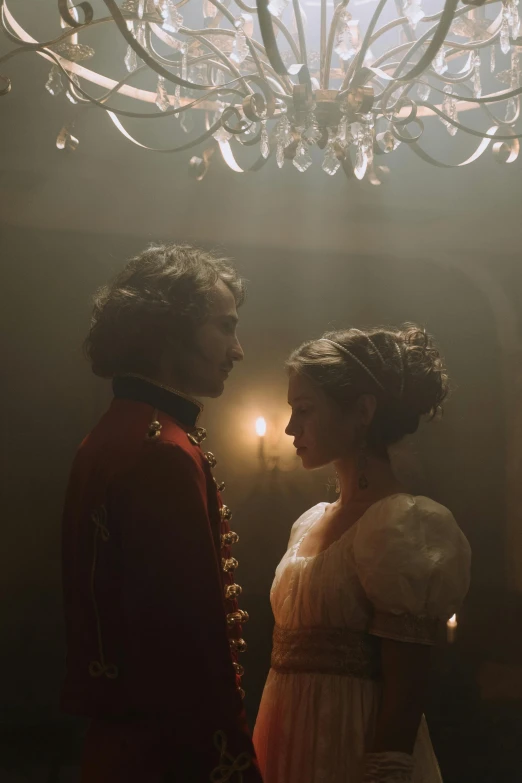 a man and a woman standing in front of a chandelier, inspired by Karl Bryullov, pexels, movie still of emma watson, cinematic back lit lighting, thick dust and red tones, historically accurate