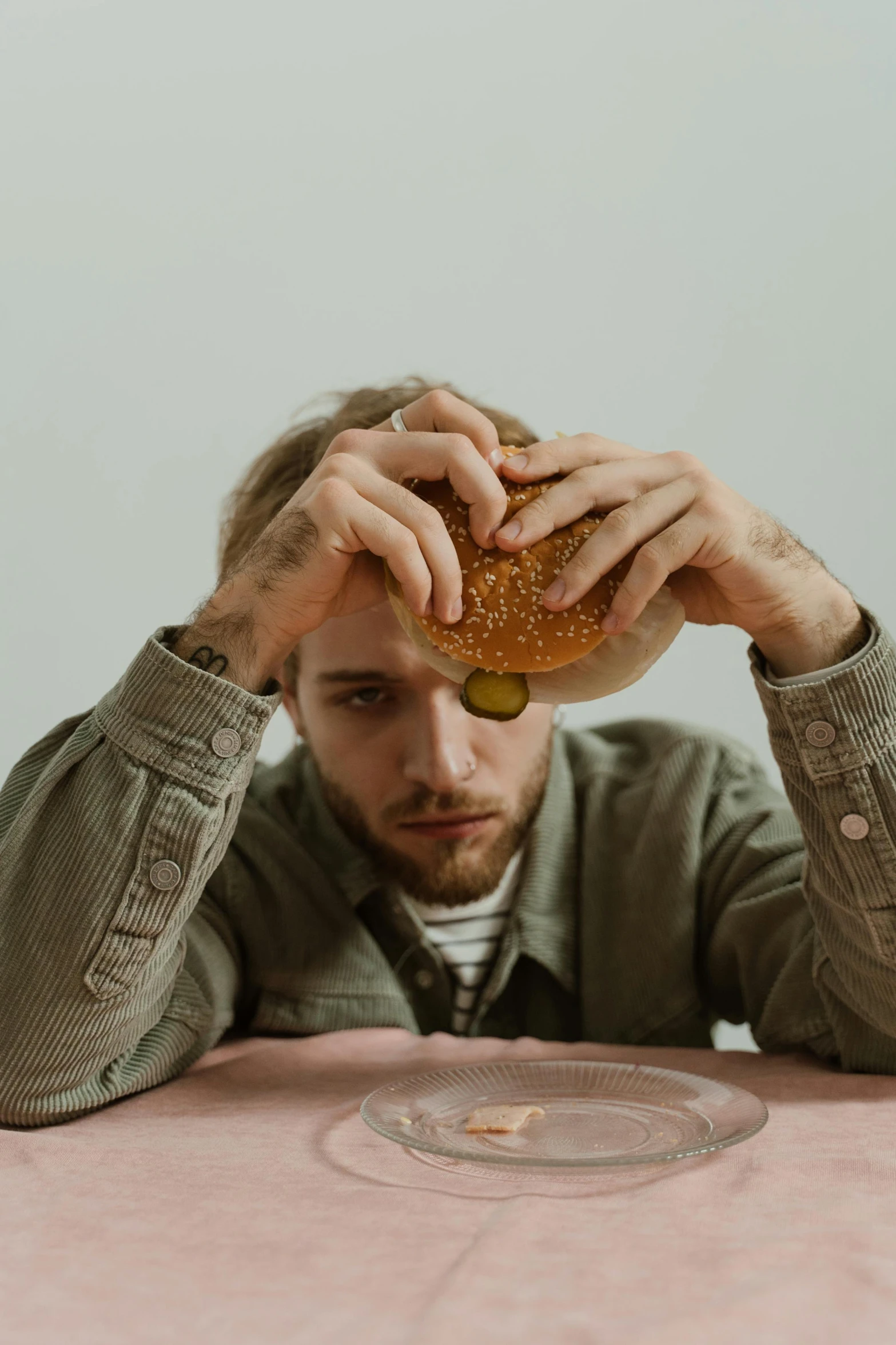a man sitting at a table with a hamburger in front of him, by Adam Marczyński, trending on pexels, a photo of a disheveled man, on a pale background, depressed mood, hozier