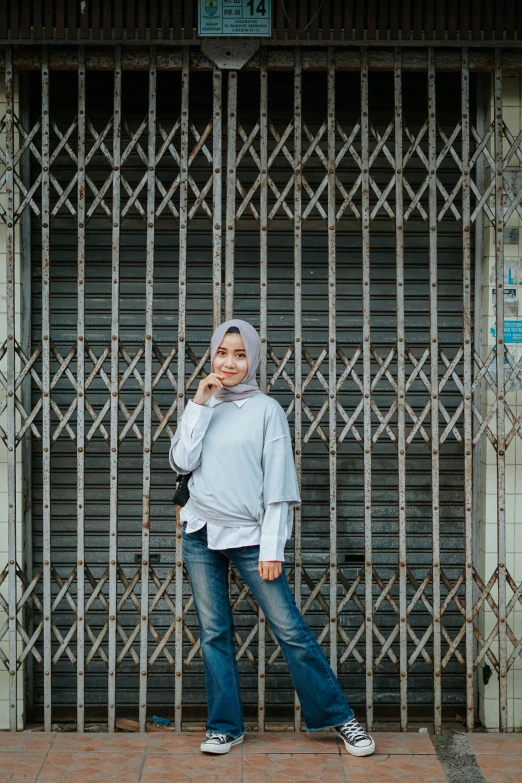 a woman standing in front of a building talking on a cell phone, by Basuki Abdullah, unsplash, hurufiyya, blue and silver colors, jeans and t shirt, cold color, background image