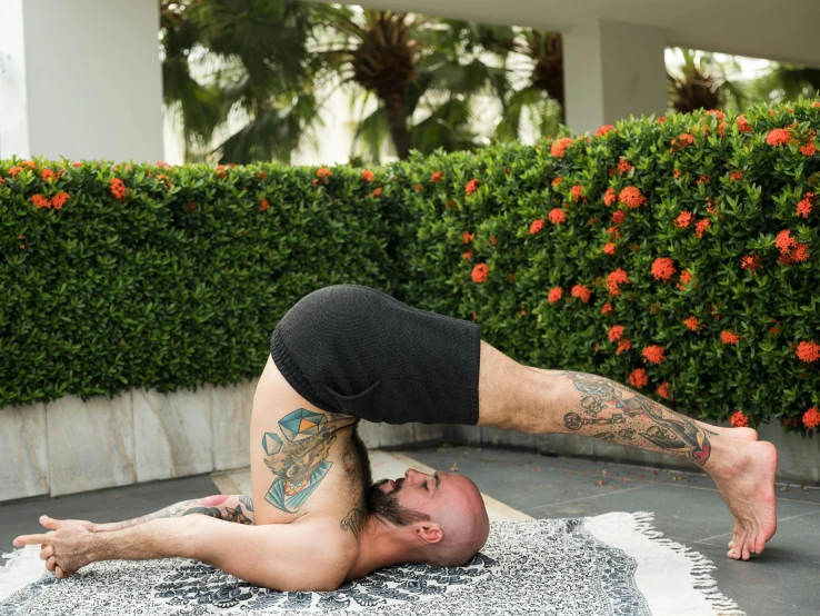 a man doing a yoga pose on a rug, arabesque, body covered in floral tattoos, nature outside, arched back, laying down