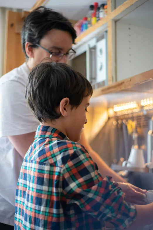 a man and a child washing dishes in a kitchen, pexels contest winner, future coder man looking on, wearing rr diner uniform, play of light, playing piano