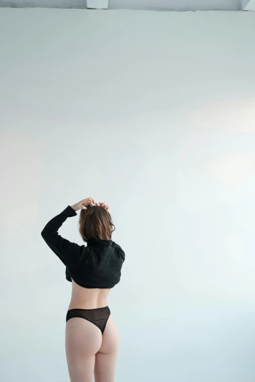 a woman in black underwear standing in front of a white wall, unsplash, looking to the sky, dancer, back - view, sheer