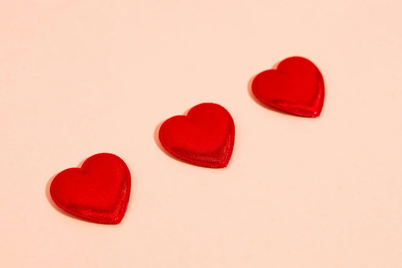 three red hearts sitting on top of a white surface, an album cover, trending on pexels, candy treatments, in red background, in a row, lined up horizontally