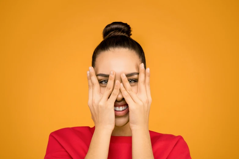 a woman covering her eyes with her hands, trending on pexels, antipodeans, silly playful fun face, very orange, press shot, instagram post