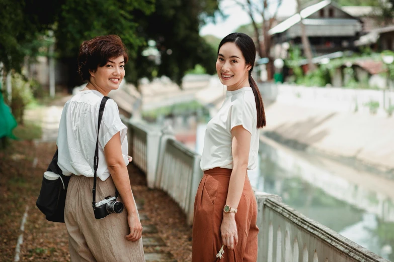 a couple of women standing next to each other, inspired by Ruth Jên, pexels contest winner, in style of thawan duchanee, looking towards camera, college, in background