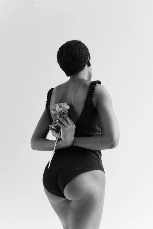 a black and white photo of a woman in a bathing suit, unsplash, renaissance, holding a flower, back view. nuri iyem, in kaethe butcher, black black black woman