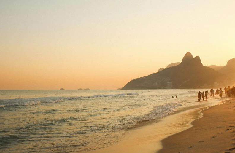 a group of people standing on top of a sandy beach, rio de janeiro, pink golden hour, nature photo