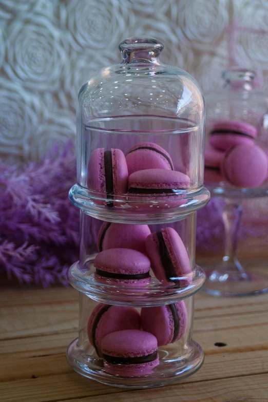 a glass jar filled with pink macarons on top of a wooden table, black and purple, stacked image, lots de details, medium