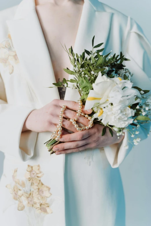 a woman in a white robe holding a bouquet of flowers, an album cover, inspired by Ruth Jên, unsplash, romanticism, pearls and gold chains, detail shot, chaumet style, modeled