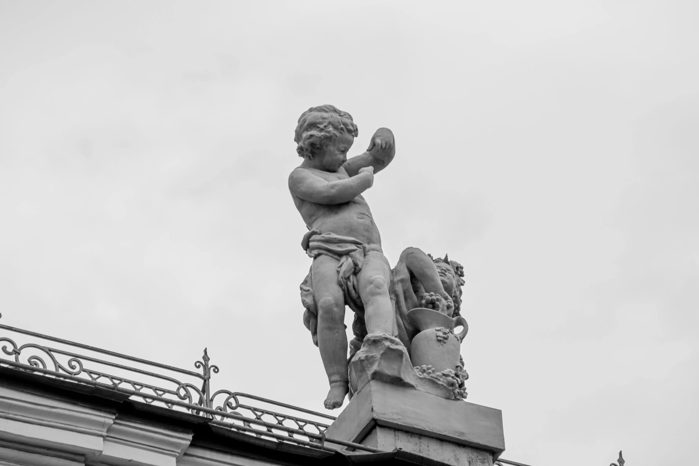 a black and white photo of a statue on top of a building, a statue, young child, baroque and rococo ornaments, with his hands in his hair, taken in the early 2020s