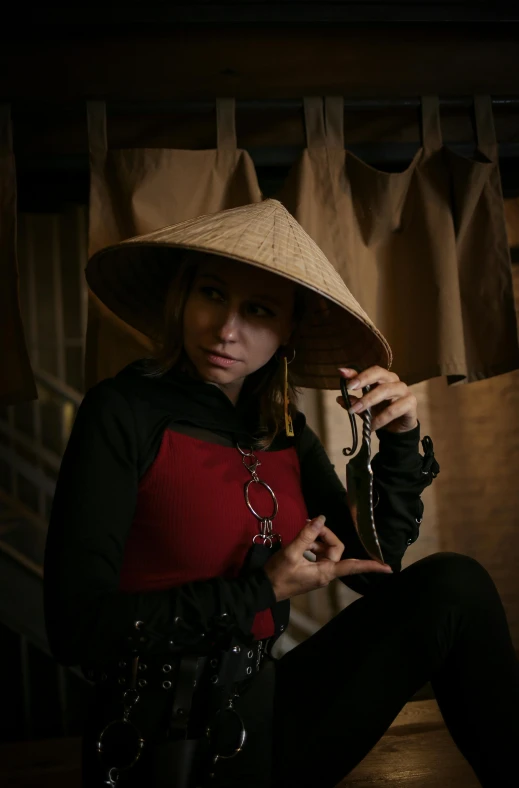 a woman sitting on a chair with a hat on, a portrait, inspired by Miao Fu, unsplash, conceptual art, ninja outfit, low quality photo, jewelry, fisting monk