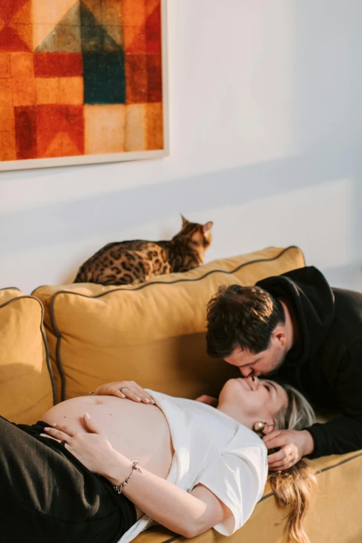 a man and woman laying on a couch next to a cat, by Julia Pishtar, pexels contest winner, visual art, pregnant belly, kissing each other, lachlan bailey, profile image