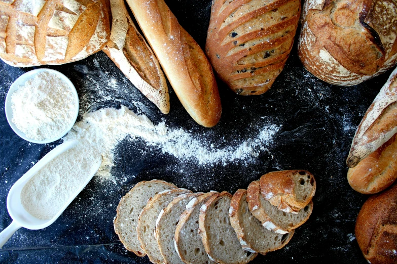 a table topped with lots of different types of bread, by Tom Wänerstrand, pexels, figuration libre, covered in white flour, on black background, background image, iphone photo