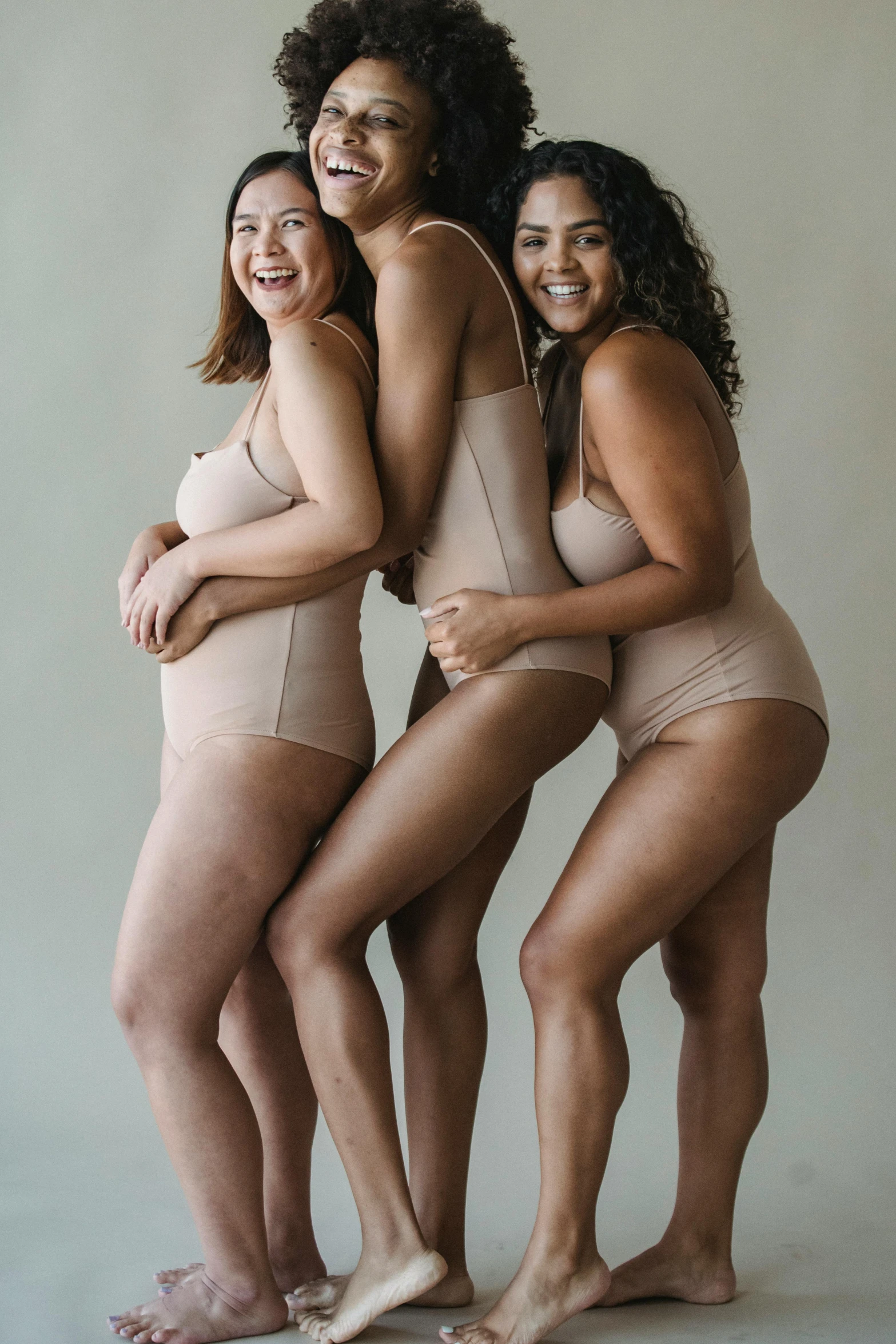 a group of women standing next to each other, by Jessie Algie, unsplash, renaissance, muted colored bodysuit, playful pose, tan complexion, underwear ad