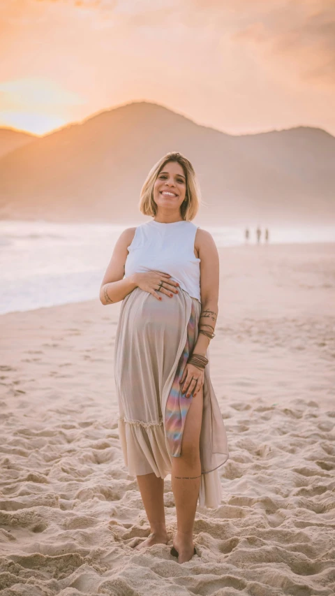 a pregnant woman standing on a beach at sunset, an album cover, inspired by Samuel Silva, pexels contest winner, happening, ana de armas portrait, long skirt, brazil, beautiful and smiling