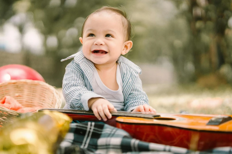 a baby sitting on top of a blanket next to a guitar, pexels contest winner, having a picnic, wide grin, avatar image, full frame image