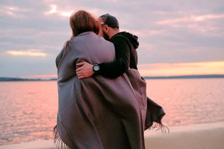 a man holding a woman wrapped in a blanket, pexels contest winner, shoreline, hugs, 1 4 9 3, manly