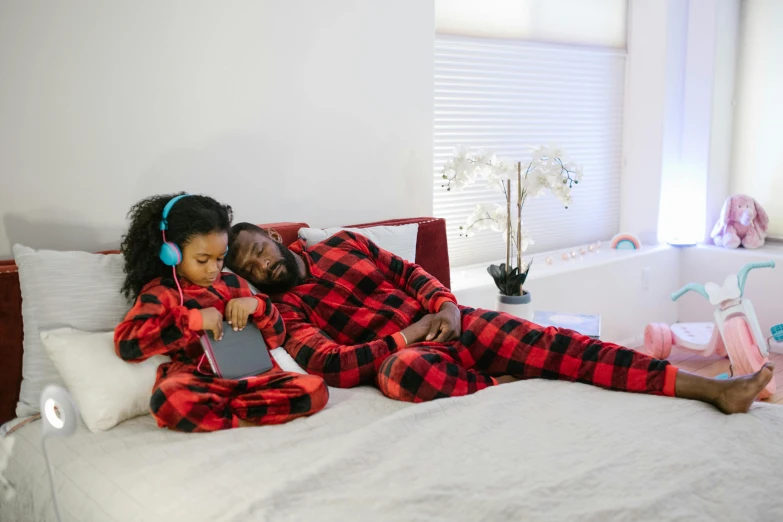 a couple of people laying on top of a bed, by Michael Gustavius Payne, pexels, red and black suit, father with child, full device, flannel