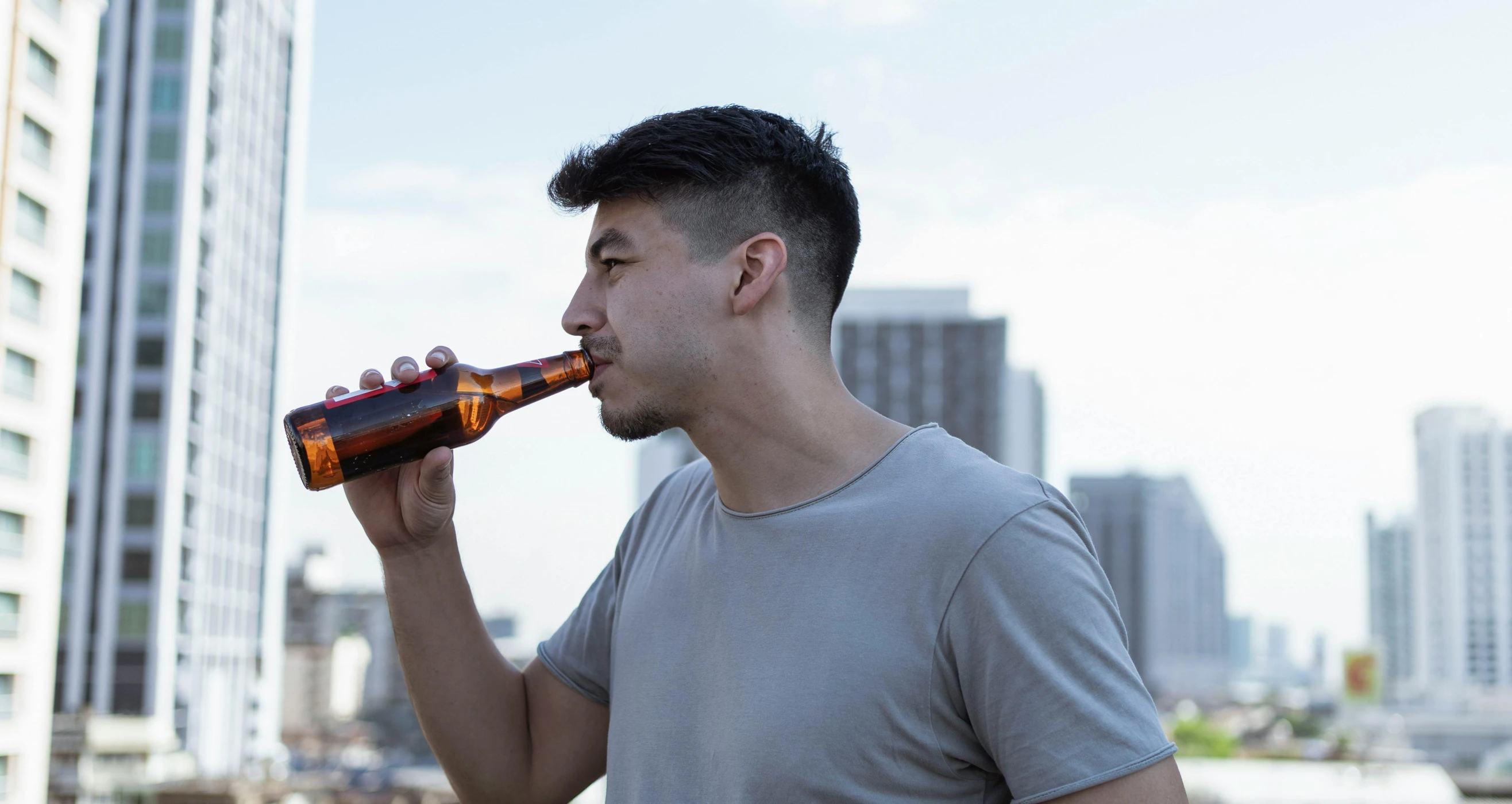 a man is drinking from a beer bottle, pexels contest winner, happening, urban in background, profile image, looking to the side off camera, brown