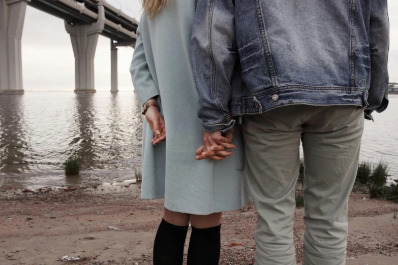 a man and a woman standing next to each other, trending on pexels, realism, under bridge, perfect hands, pastel clothing, coastal