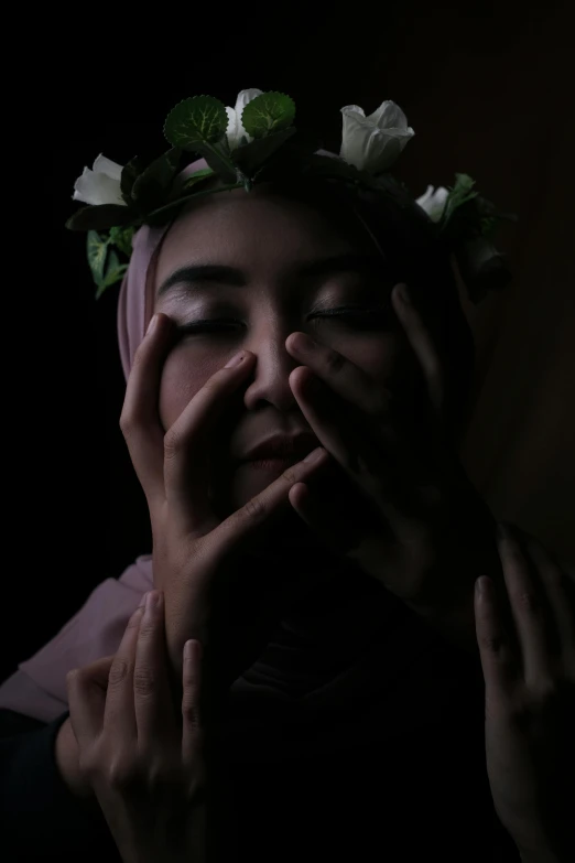 a woman with a flower crown covering her face, a picture, inspired by irakli nadar, pexels contest winner, aestheticism, hijab, ( low key light ), holding his hands up to his face, ((portrait))