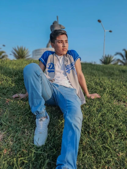 a man sitting on top of a lush green field, an album cover, by Ahmed Yacoubi, unsplash, happening, blue pants, non binary model, in egypt, ((blue))
