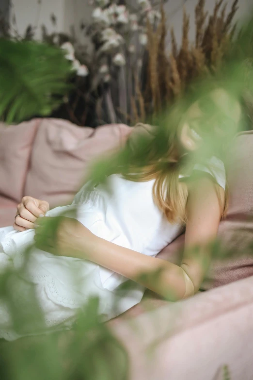 a woman laying on top of a pink couch, by Alice Mason, unsplash, lush greenery, wearing white cloths, linen, blur dreamy outdoor