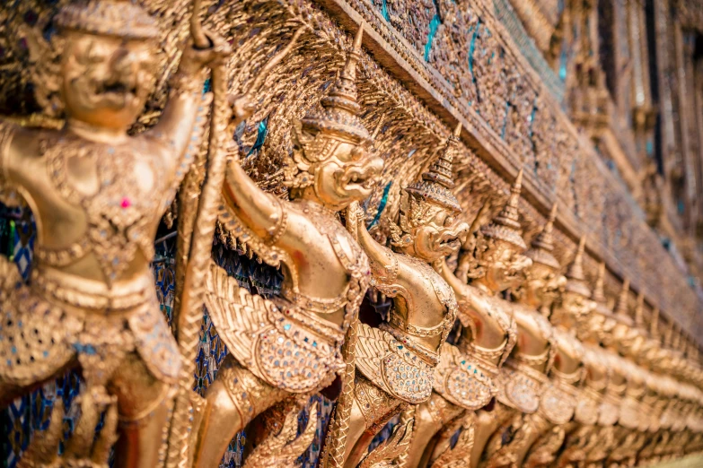 a group of gold statues on the side of a building, by Tom Wänerstrand, pexels contest winner, thai, ornate gold border, guards intricate, thumbnail