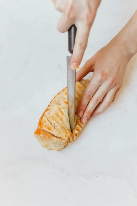 a person cutting a piece of food with a knife, holding a baguette, from the side, top down angle, stainless steal