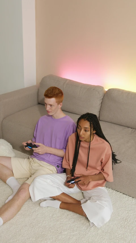 two people sitting on the floor playing a video game, by Carey Morris, pexels, realism, toned orange and pastel pink, on a couch, non binary model, pastel clothing