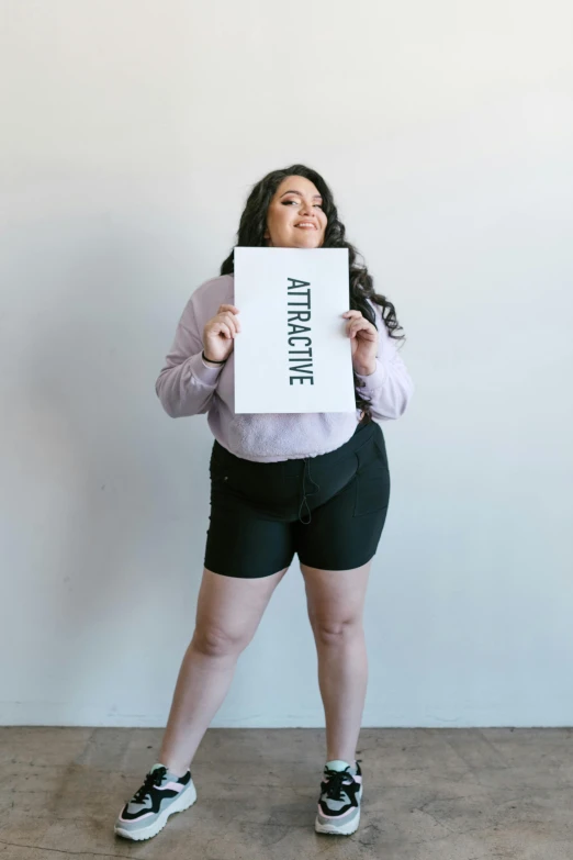 a woman holding a sign in front of her face, trending on unsplash, auto-destructive art, wearing black shorts, alluring plus sized model, « attractive, her wardrobe is attractive
