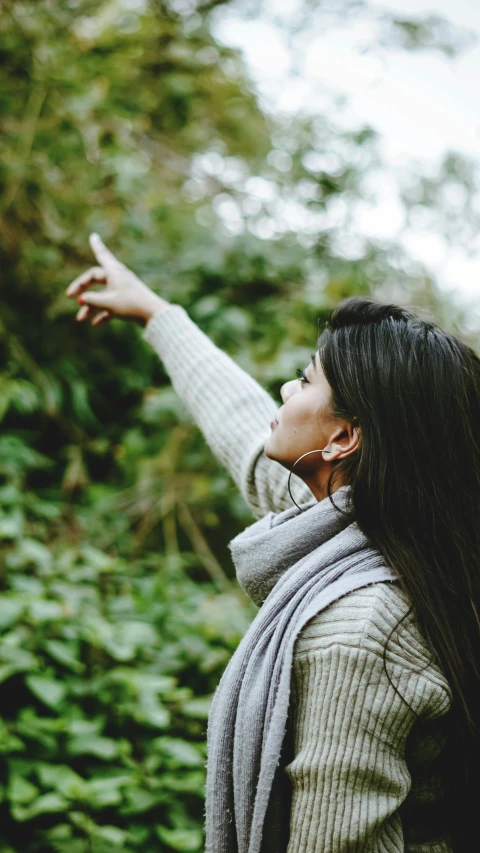 a woman pointing at something in the air, pexels, lush surroundings, profile perspective, grey, digital still