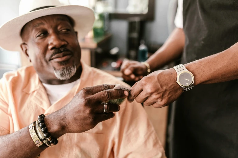 a man in a hat is cutting another man's hair, by Dan Frazier, trending on pexels, intricate african jewellery, old gigachad with grey beard, holding gold watch, snoop dog