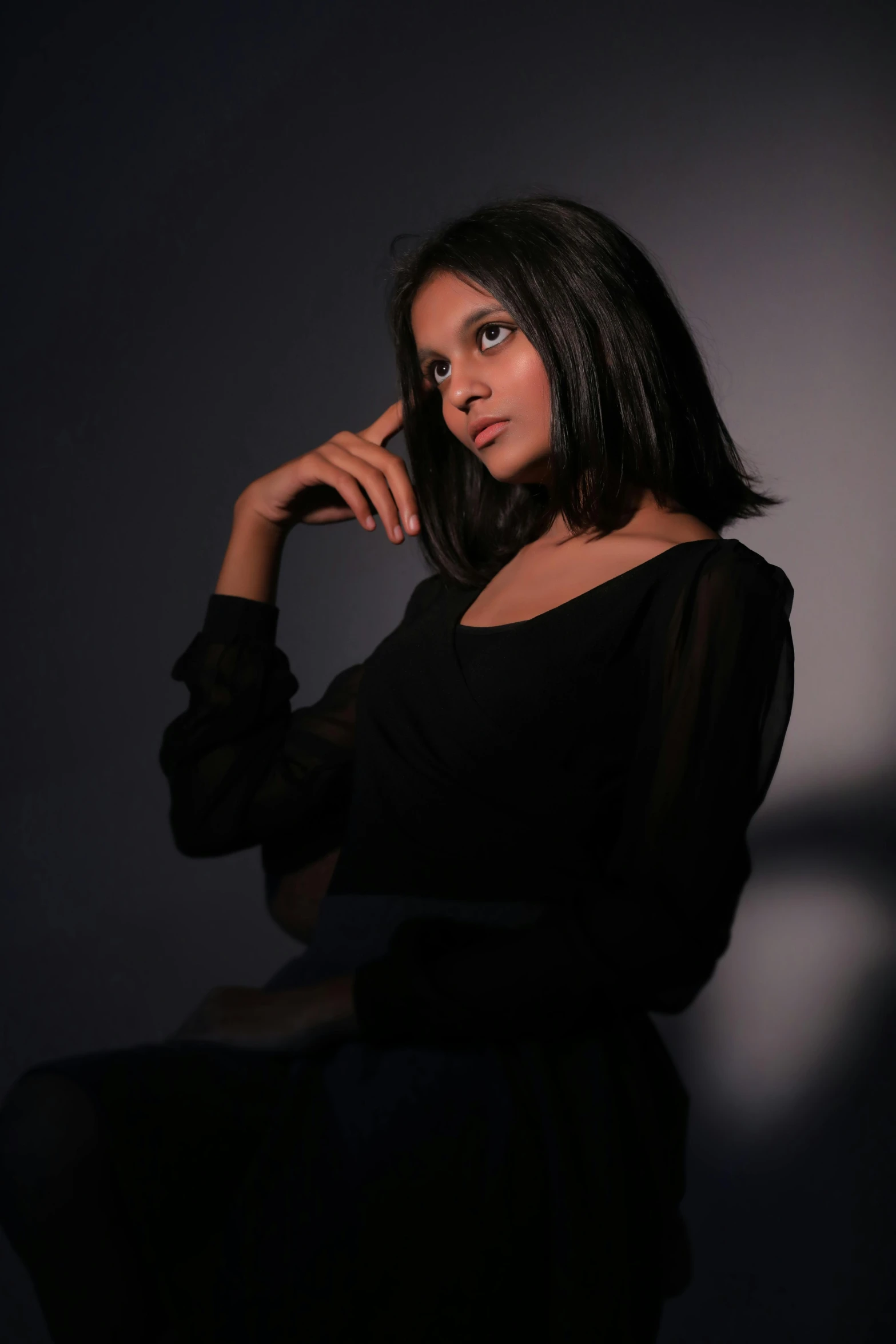 a woman sitting on a chair in a dark room, an album cover, inspired by Yousuf Karsh, pexels contest winner, indian girl with brown skin, medium format. soft light, candid!! dark background, headshot profile picture