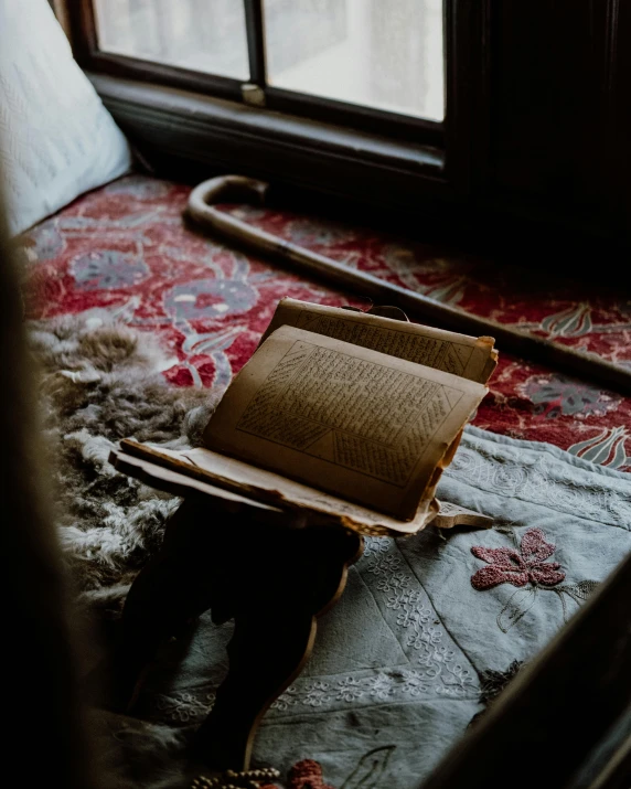 an open book sitting on top of a bed next to a window, by Elsa Bleda, unsplash contest winner, arts and crafts movement, wearing 1 8 5 0 s clothes, religious, from reading to playing games, winter