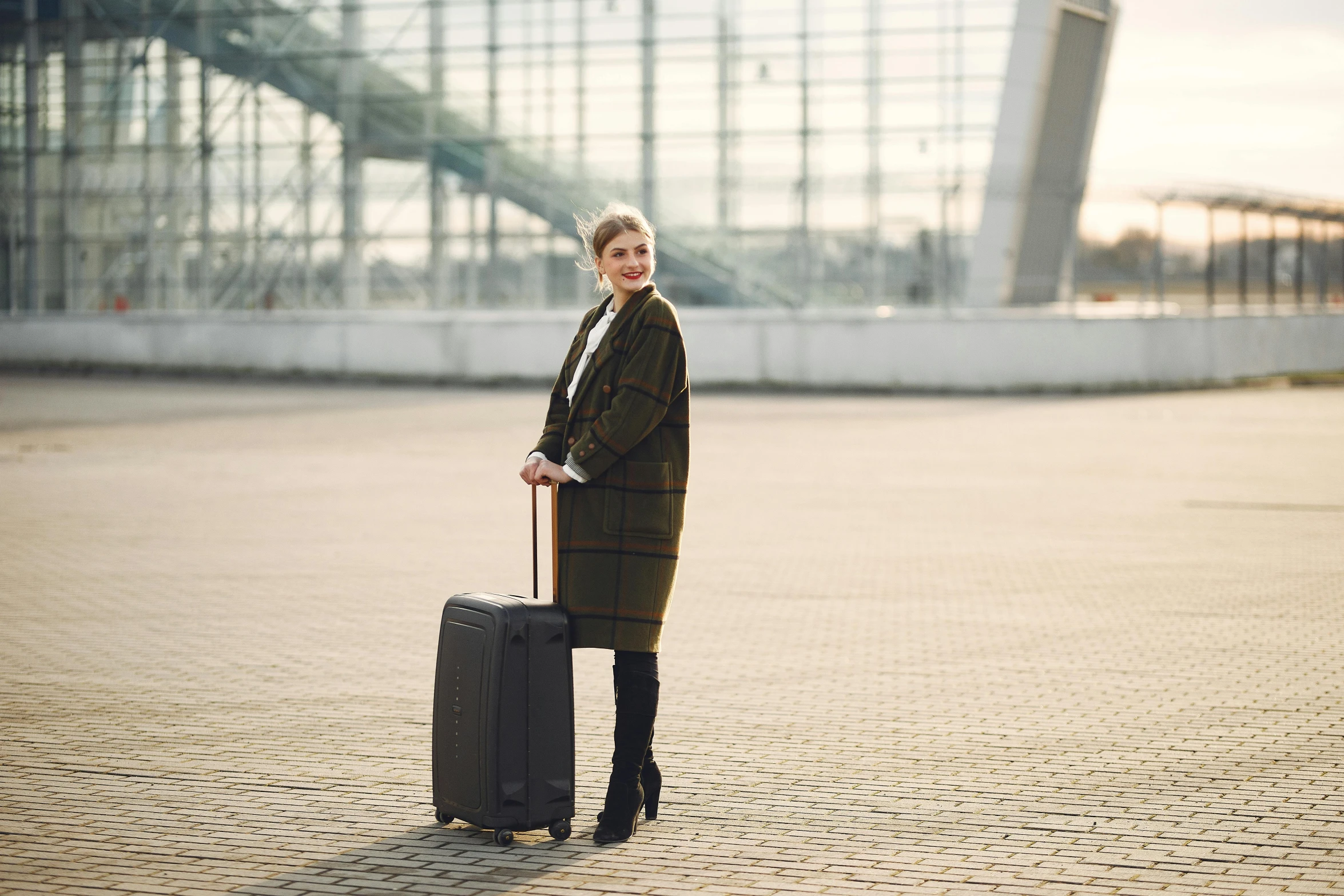 a woman standing with a suitcase in front of a building, airport, wearing a long coat, professional photo, thumbnail