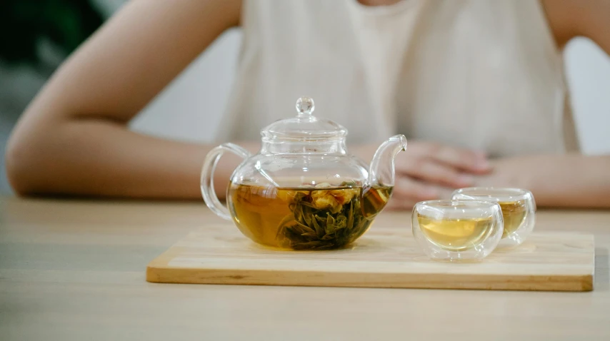 a woman sitting at a table with a cup of tea and a teapot, inspired by Zeng Jing, trending on unsplash, glass jar, on a wooden plate, white, close-up product photo