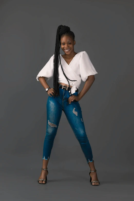 a woman standing with her hands on her hips, by Chinwe Chukwuogo-Roy, pexels contest winner, white shirt and blue jeans, dramatic smiling pose, with black pigtails, ripped jeans