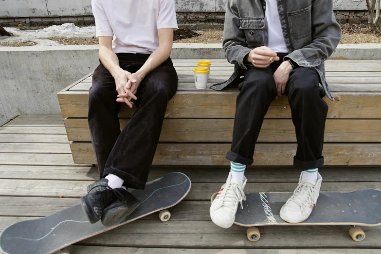 two people sitting on a bench with skateboards, trending on pexels, very pale, dardenne brothers, wearing pants, federation clothing