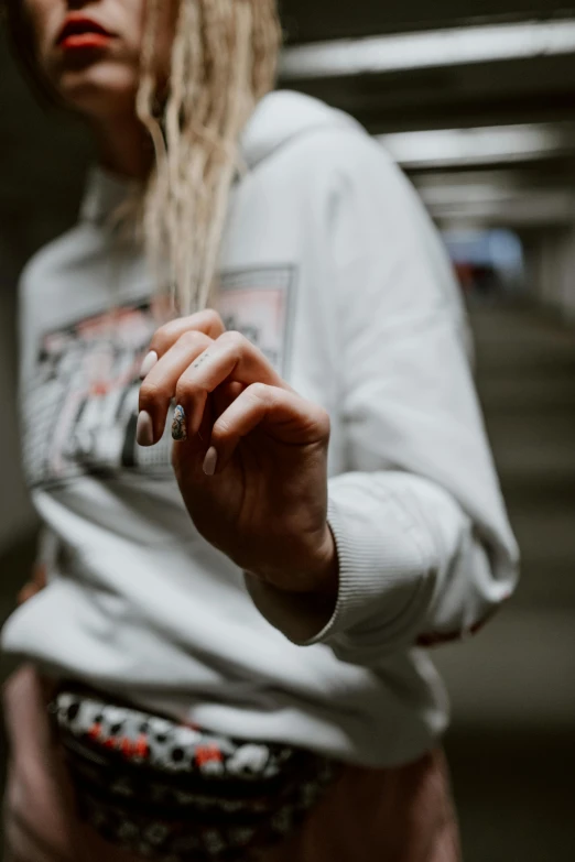 a woman standing in a parking garage holding a cigarette, inspired by Elsa Bleda, trending on pexels, graffiti, grey sweater, unclipped fingernails, dressed in a white t-shirt, trending on r/streetwear