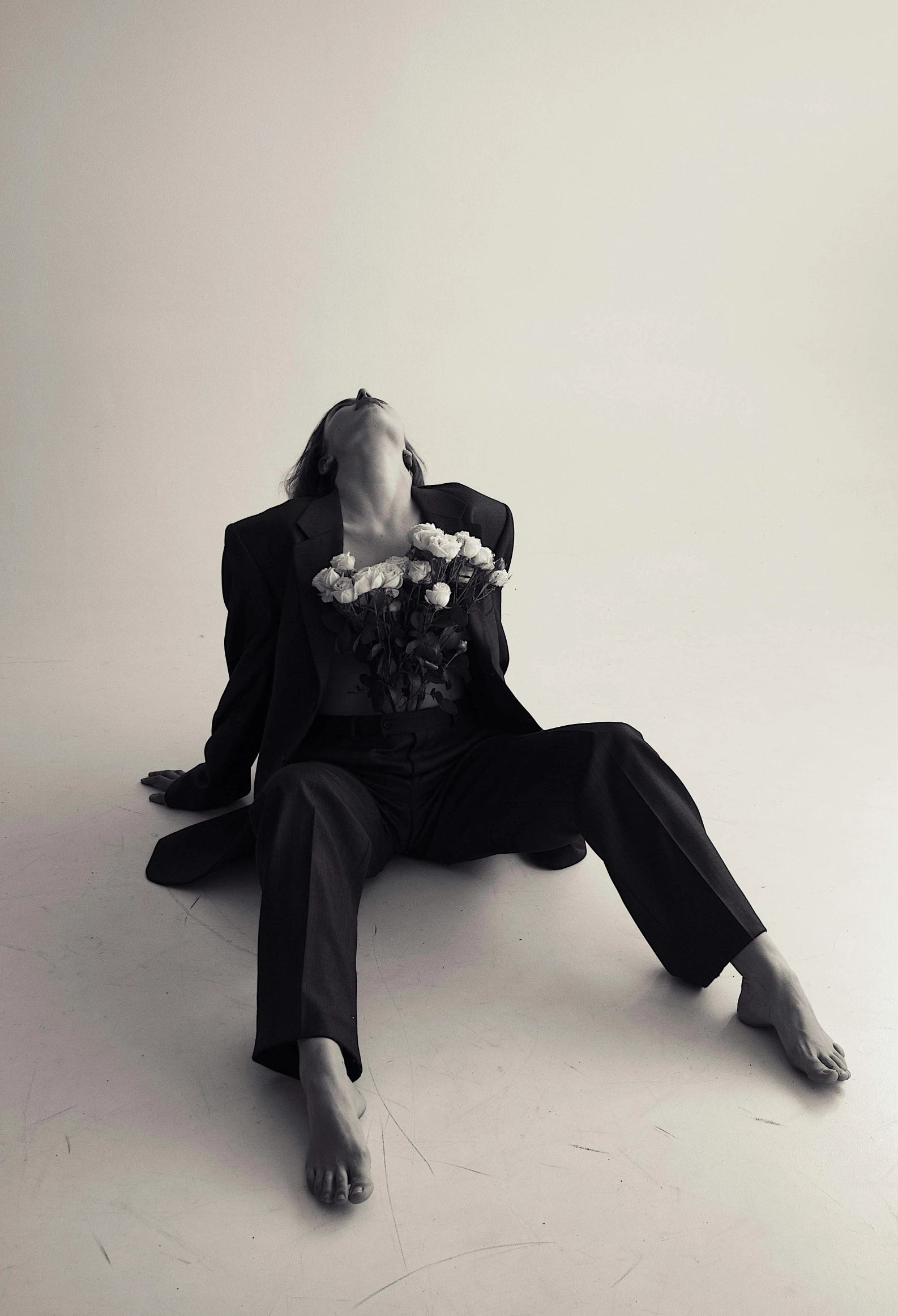 a man sitting on the ground holding a bunch of flowers, an album cover, inspired by Bert Stern, neo-figurative, black suit, claudia black, monochrome, johan liebert