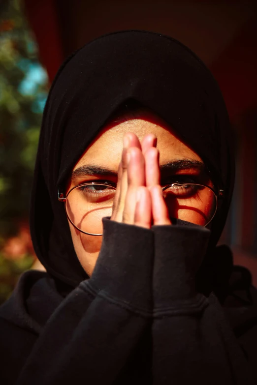 a woman with glasses covering her face with her hands, an album cover, by Ibrahim Kodra, trending on unsplash, hurufiyya, pointed hoods, at college, ((portrait)), hindu aesthetic