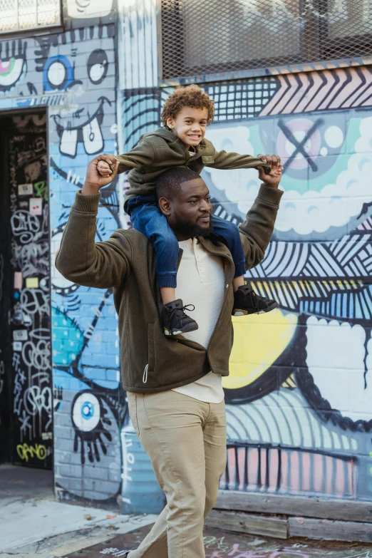 a man carrying a little boy on his shoulders, by Washington Allston, pexels contest winner, symbolism, graffiti in background, kevin hart, handsome man, burly